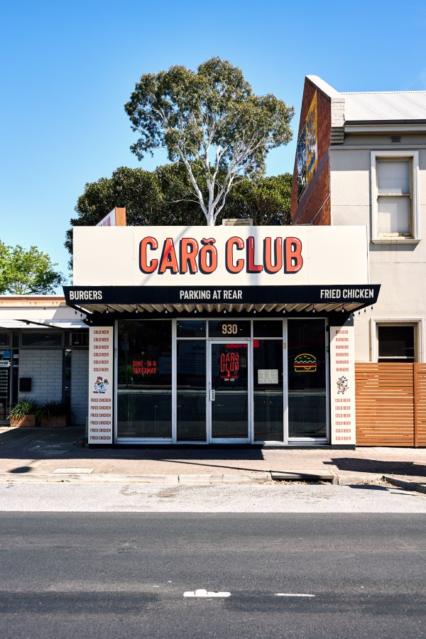Image of the shopfront view of CAROclub's new Edwardstown store, with their logo in red text on a white background above the doots to enter the shop. The doors have neon burger signs in the windows. 
