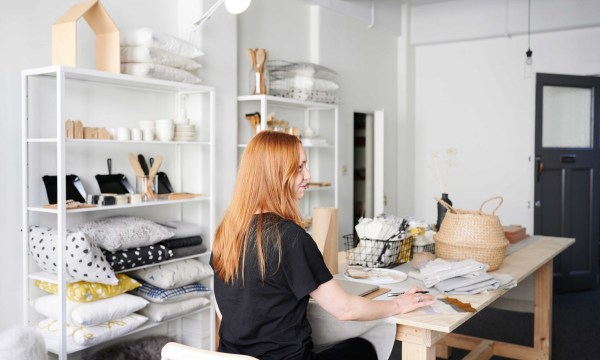 Owner of Kin Studios, Kiah Gardiner is in the centre of the image at her desk designing new linen concepts for her store.