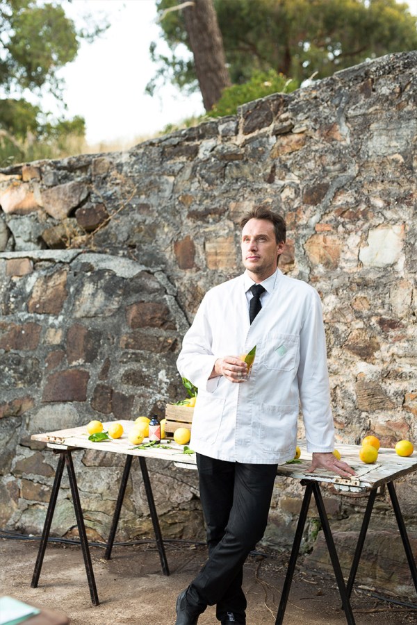 Matt Bax wears an old-fashioned white overcoat in the fashion of a bartender, while holding a cocktail